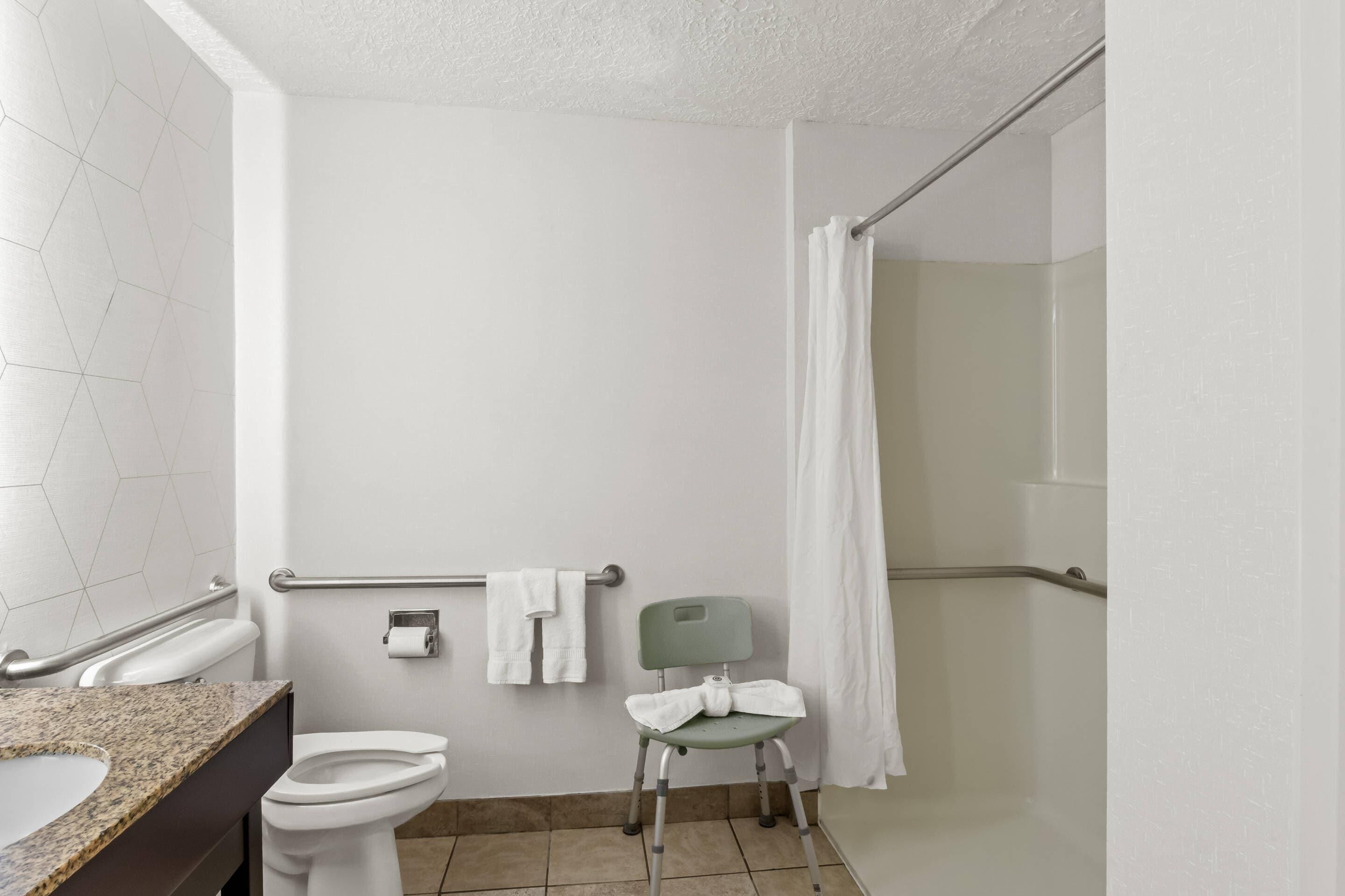 Een badkamer met toilet, wastafel, douche met gordijn en een stoel.