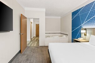 A hotel room with a bed, a bathroom with a bathtub, a desk with a phone, and a TV mounted on the wall.