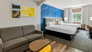 A hotel room with a sofa, two beds, a desk, and artwork on the walls. - Comfort Suites Clackamas (Clackamas)