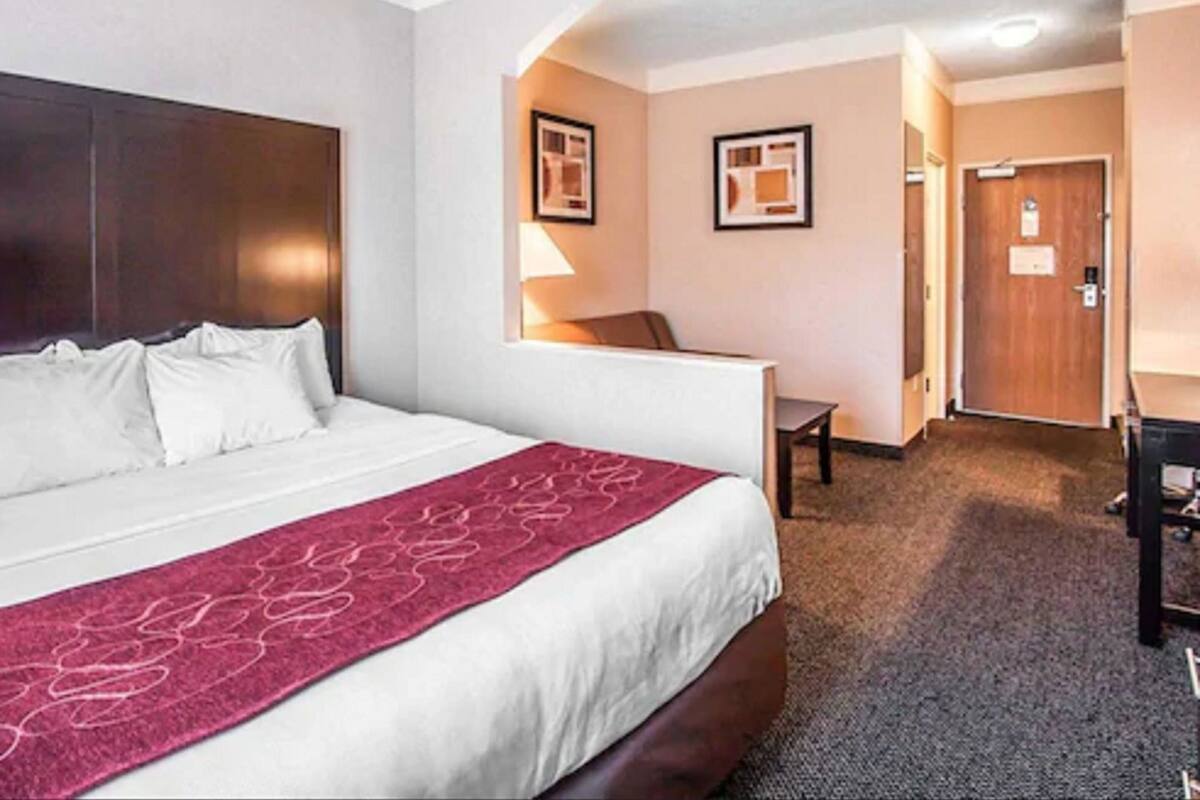 A hotel room with a bed, a desk, a chair, and a door.