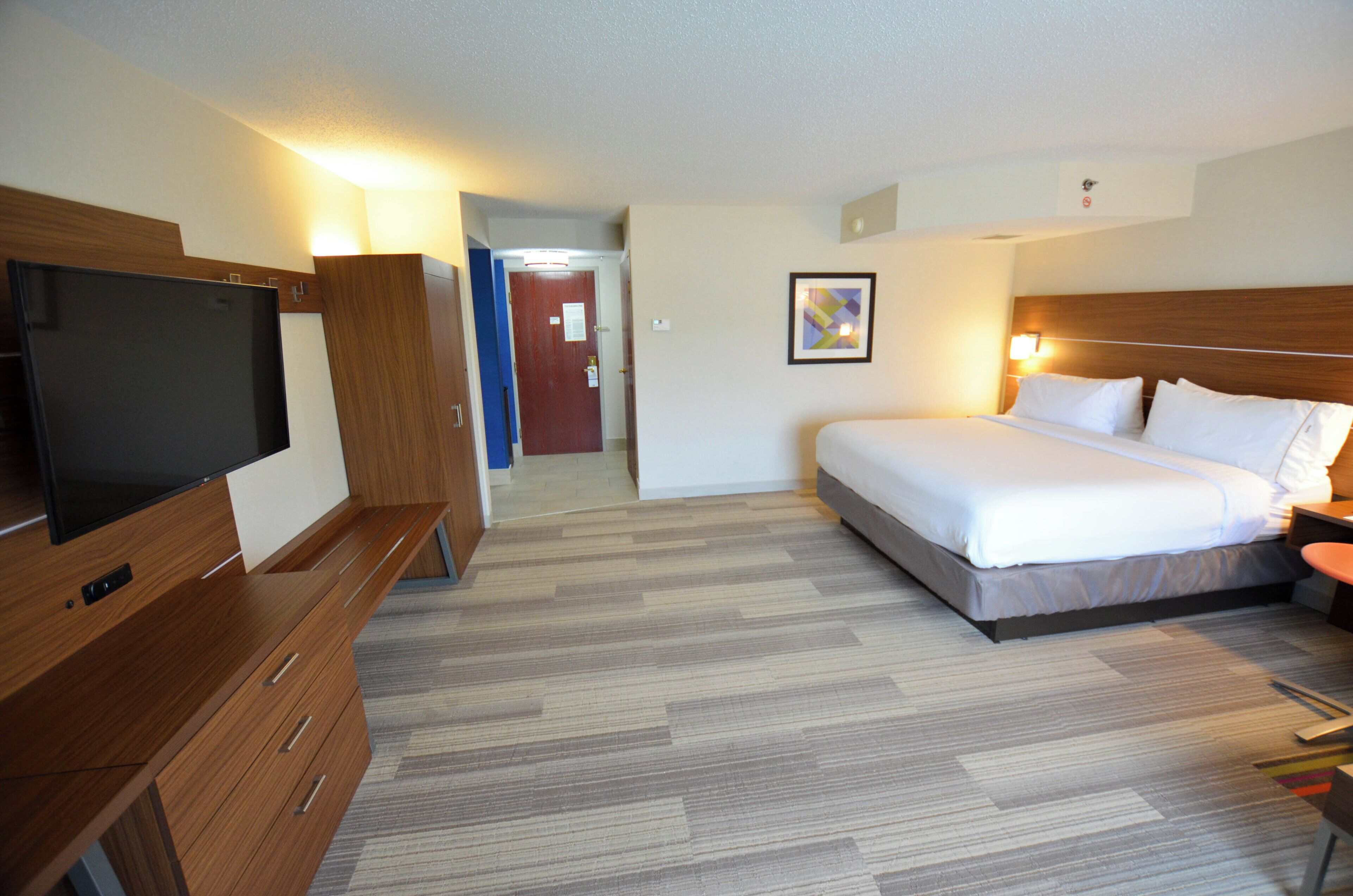 A hotel room with a bed, a television, a desk, and a door leading to another room.