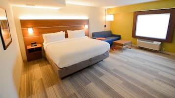 A hotel room with a large bed, a small sofa, a nightstand, and a desk.