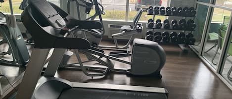 Un gimnasio con cintas de correr, una bicicleta estática y un estante de mancuernas.
