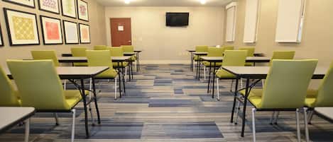 Un salón de conferencias con mesas y sillas, un televisor de pantalla plana en la pared y cuadros colgados en la pared.