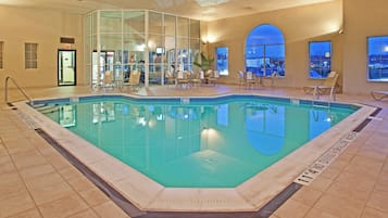 Una piscina interior con agua cristalina, rodeada de sillones de descanso y un muro de vidrio.