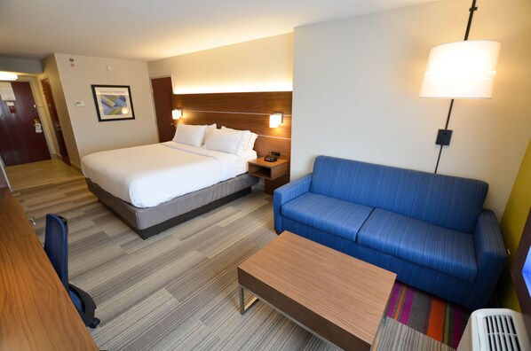 A hotel room with a bed, a blue sofa, a wooden coffee table, and a desk with a chair. - Holiday Inn Express Pittsburgh-Bridgeville by IHG (Bridgeville)