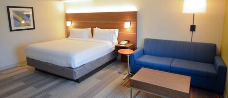 A hotel room with a bed, a blue sofa, a small table, and a nightstand with a lamp.