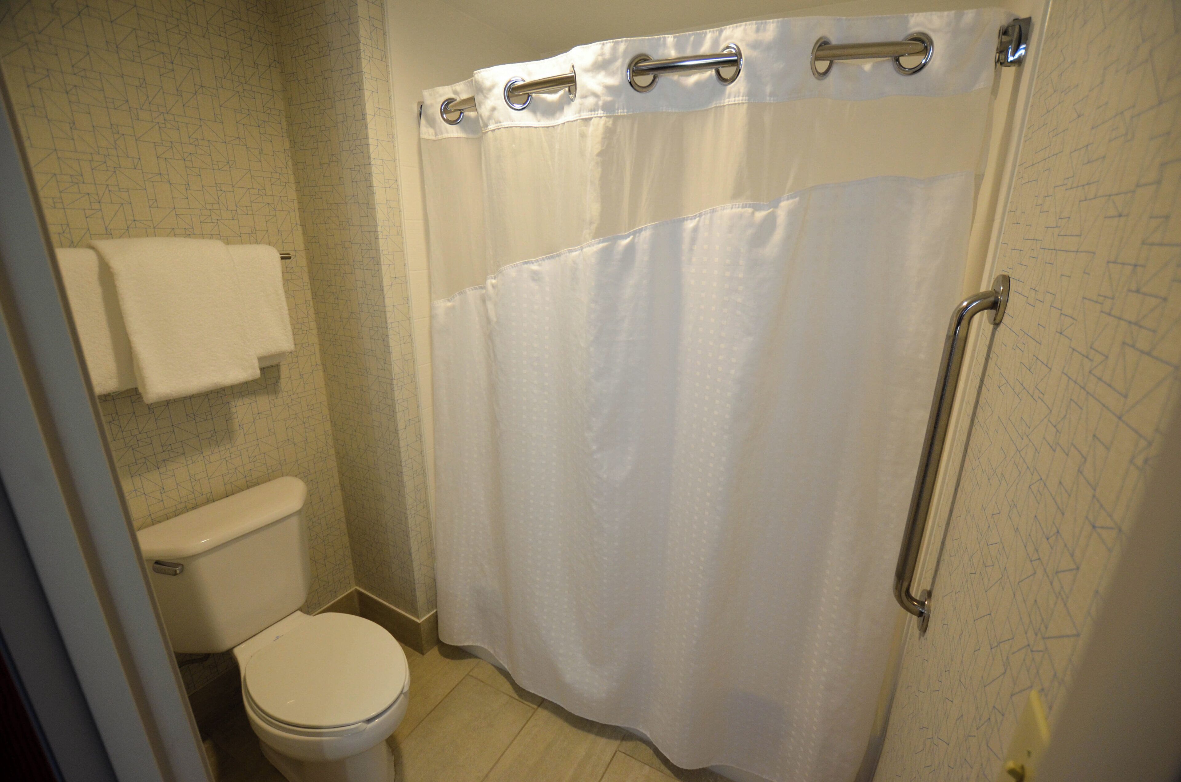 Un baño con inodoro, cortina de ducha y una toalla colgada en la pared.