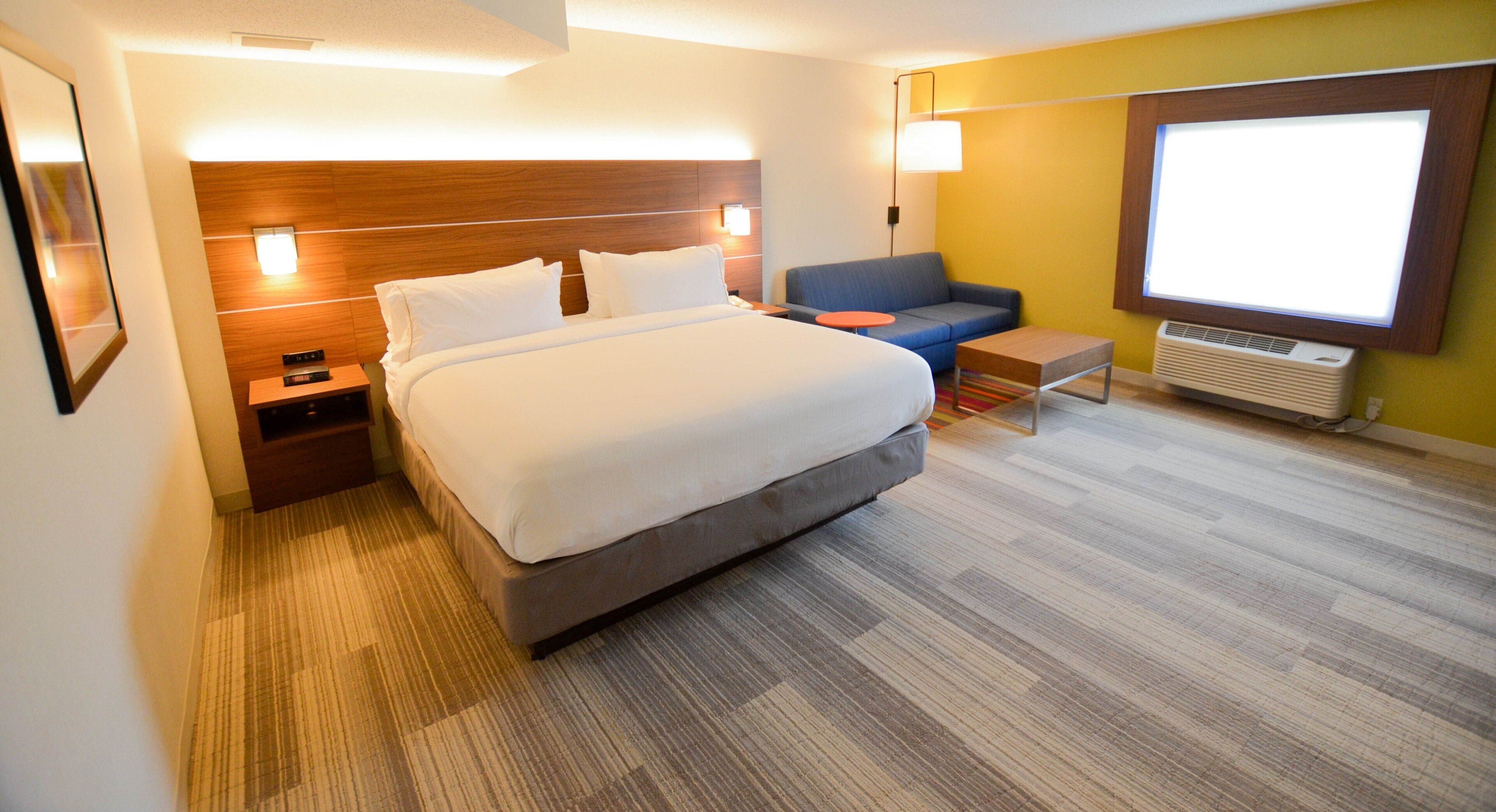 A hotel room with a large bed, a sofa, a small table, and a window.