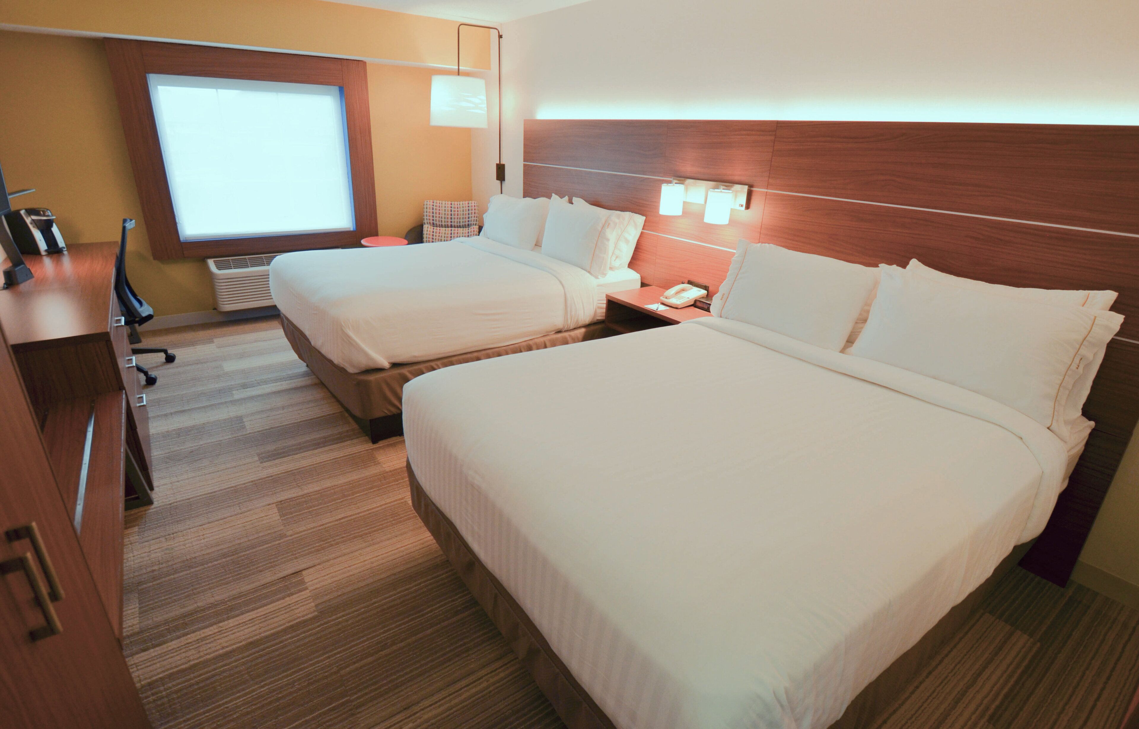A hotel room with two beds, a desk, a chair, a desk lamp, a telephone, and a window with blinds.