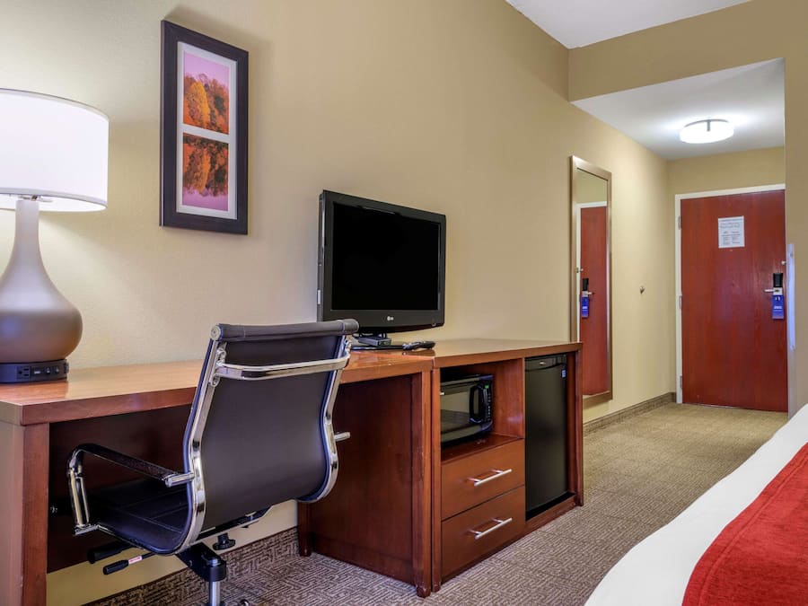 A hotel room with a desk, chair, television, and a microwave.