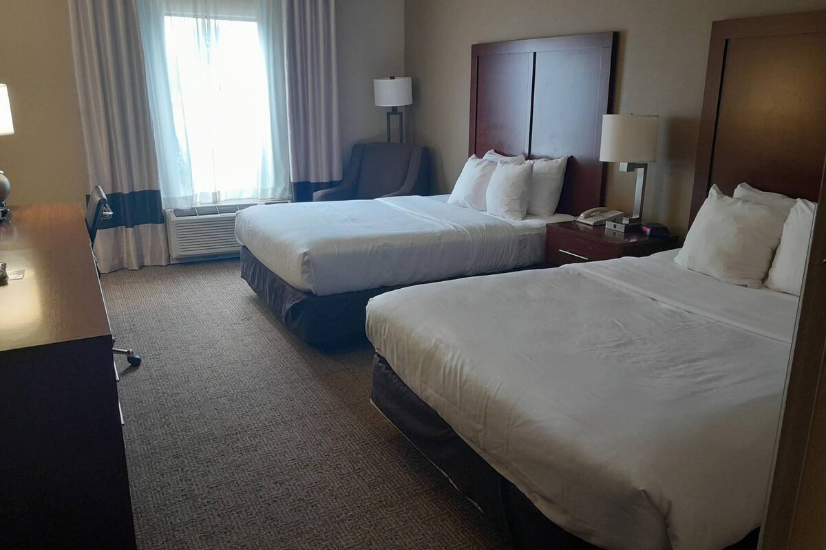 A hotel room with two beds, a desk, a chair, a lamp, and a nightstand.