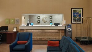A reception desk with computers, a fireplace, a blue armchair, a blue sofa, and a trash bin. - Comfort Inn Duncansville - Altoona (Hollidaysburg)