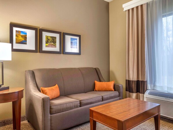 A hotel room with a grey sofa, two orange cushions, a wooden coffee table, and three framed pictures on the wall.