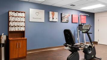 A fitness room with a treadmill, a cabinet with towels, and motivational wall art.