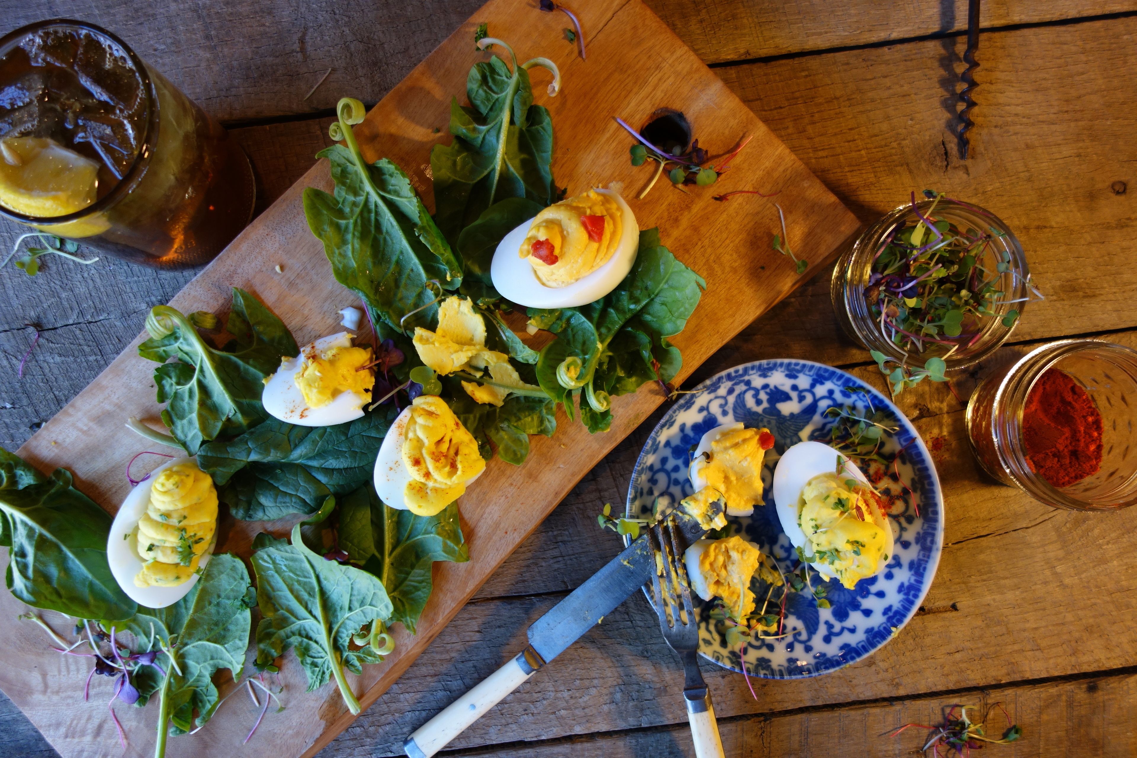 A wooden table with a plate of deviled eggs, a bowl of greens, and a glass of red wine.