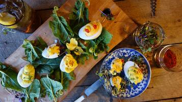 A wooden table with a plate of deviled eggs, a bowl of greens, and a glass of red wine.