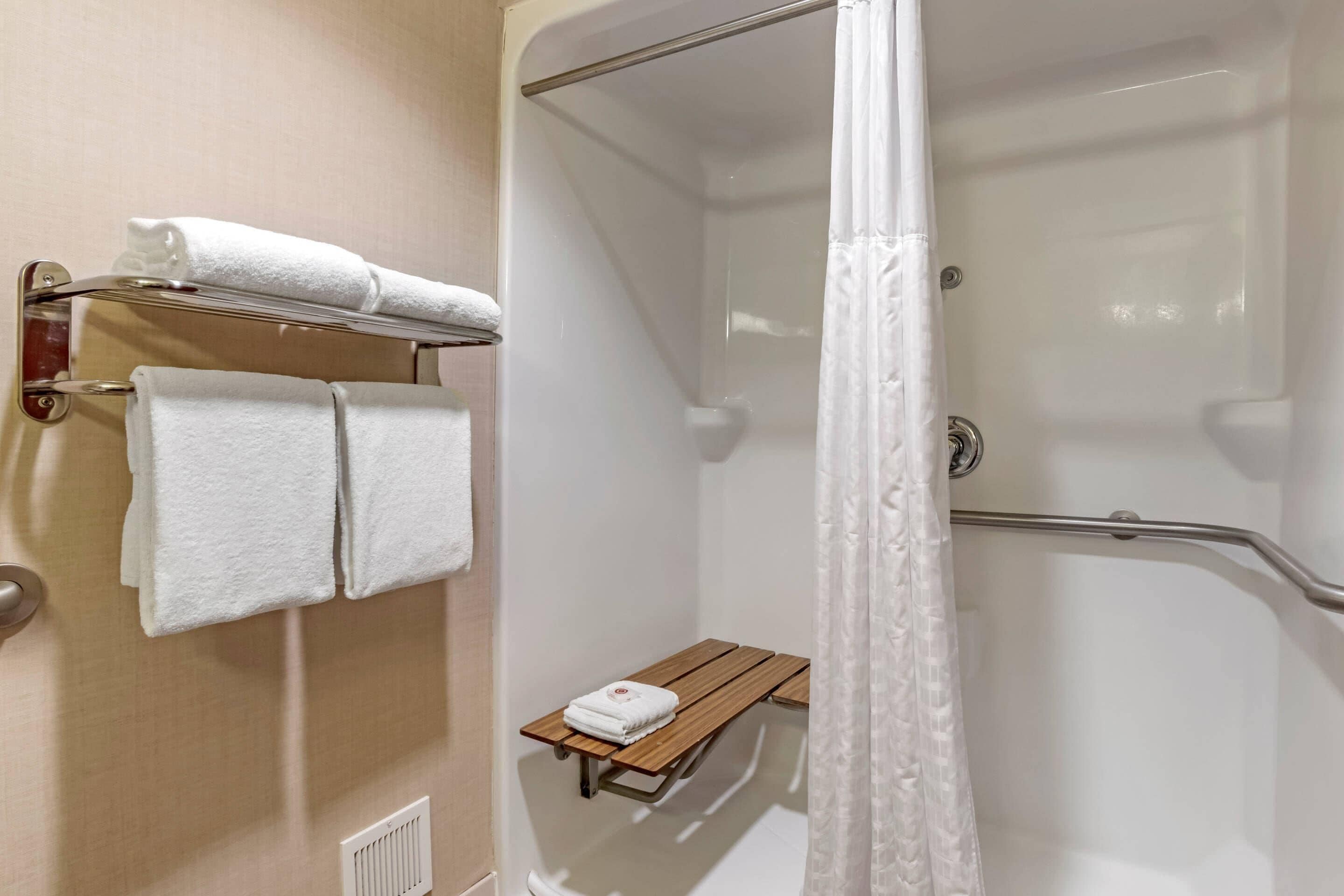 A shower area with a glass door, a towel rack with towels, and a wooden bench.