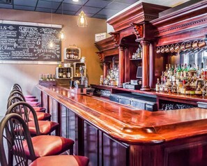 Un bar con mostrador de madera pulida, un menú en pizarra y una variedad de botellas de licor.