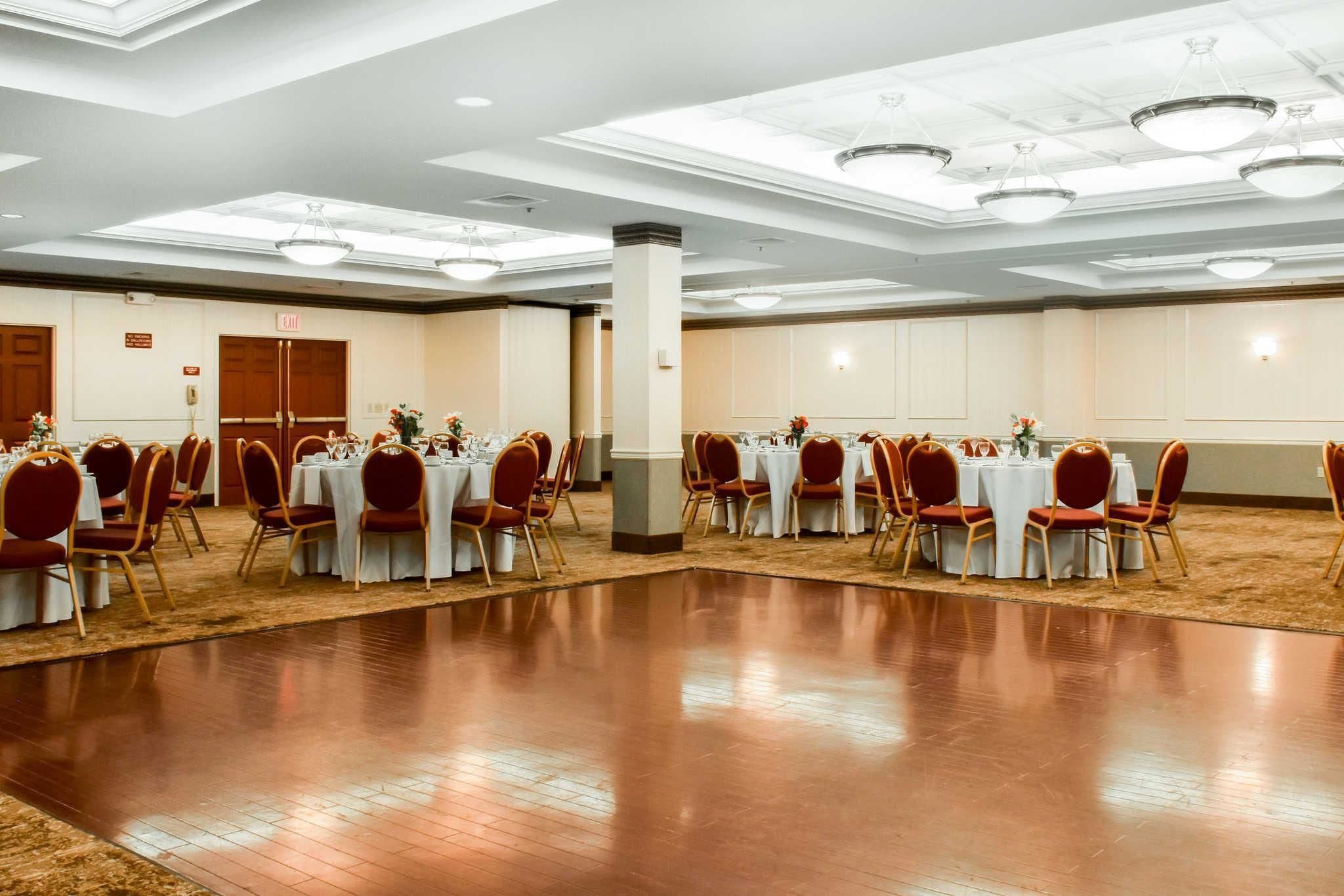 Un amplio y luminoso salón de banquetes con varias mesas redondas y sillas, un piso de madera pulida y un techo alto con iluminación empotrada.