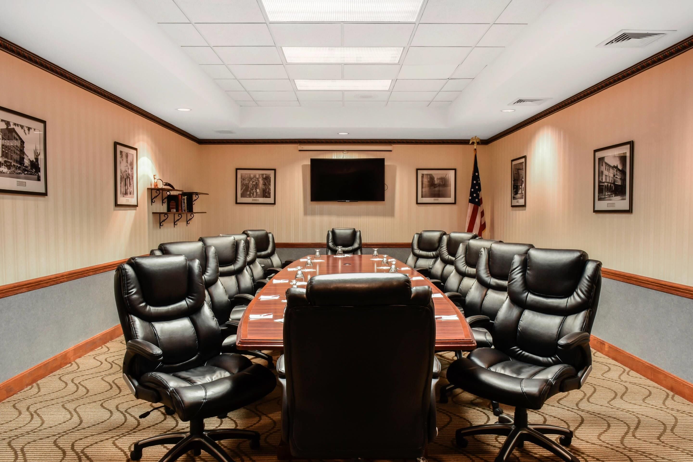 A conference room with a long table, black leather chairs, framed pictures on the walls, and an American flag.