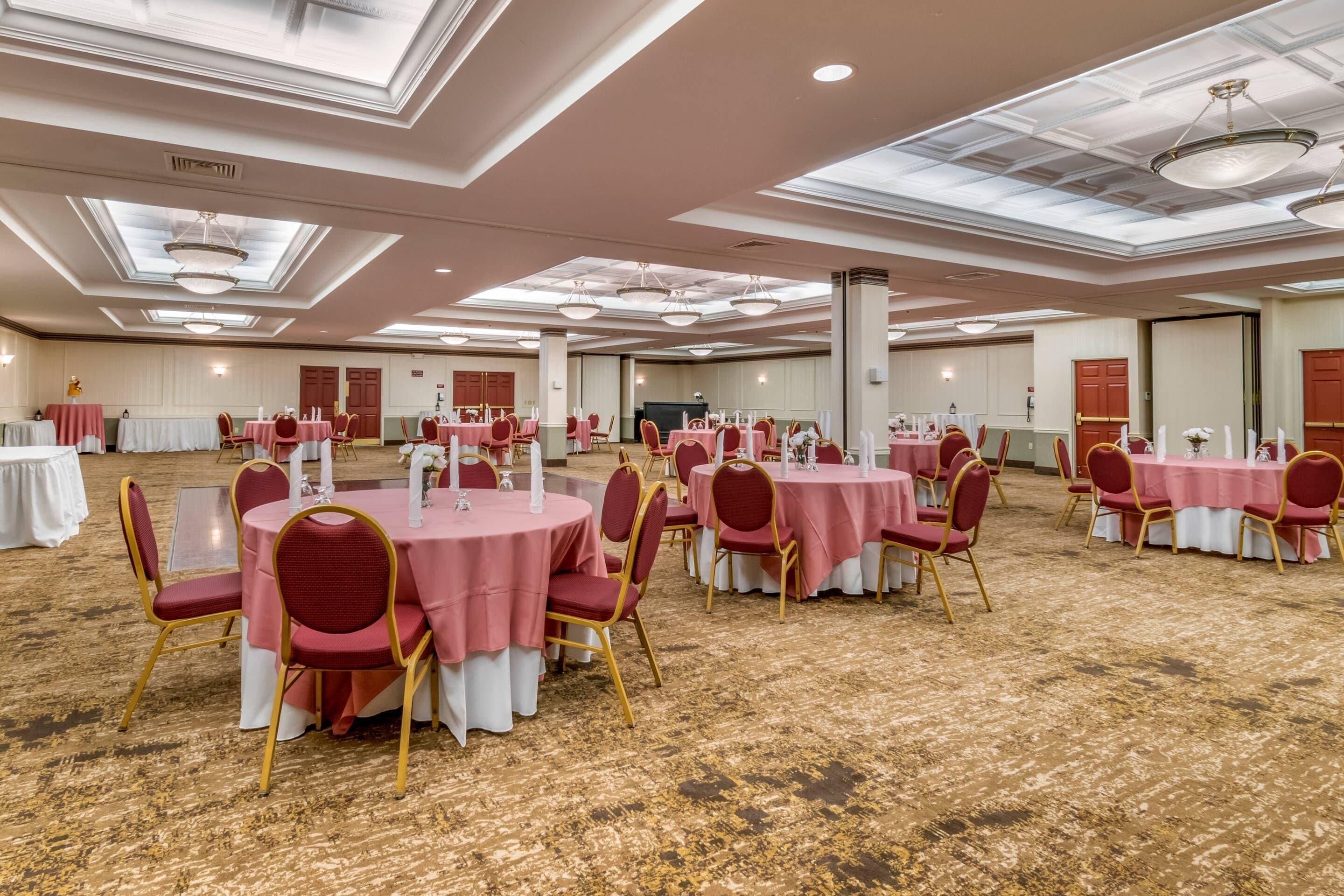 Un salón de banquetes con mesas redondas cubiertas con manteles rosas, sillas rojas y velas blancas.