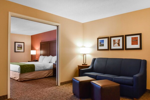 Habitación de hotel con una cama, un sofá azul, una mesita y una lámpara. En la pared hay cuadros enmarcados.