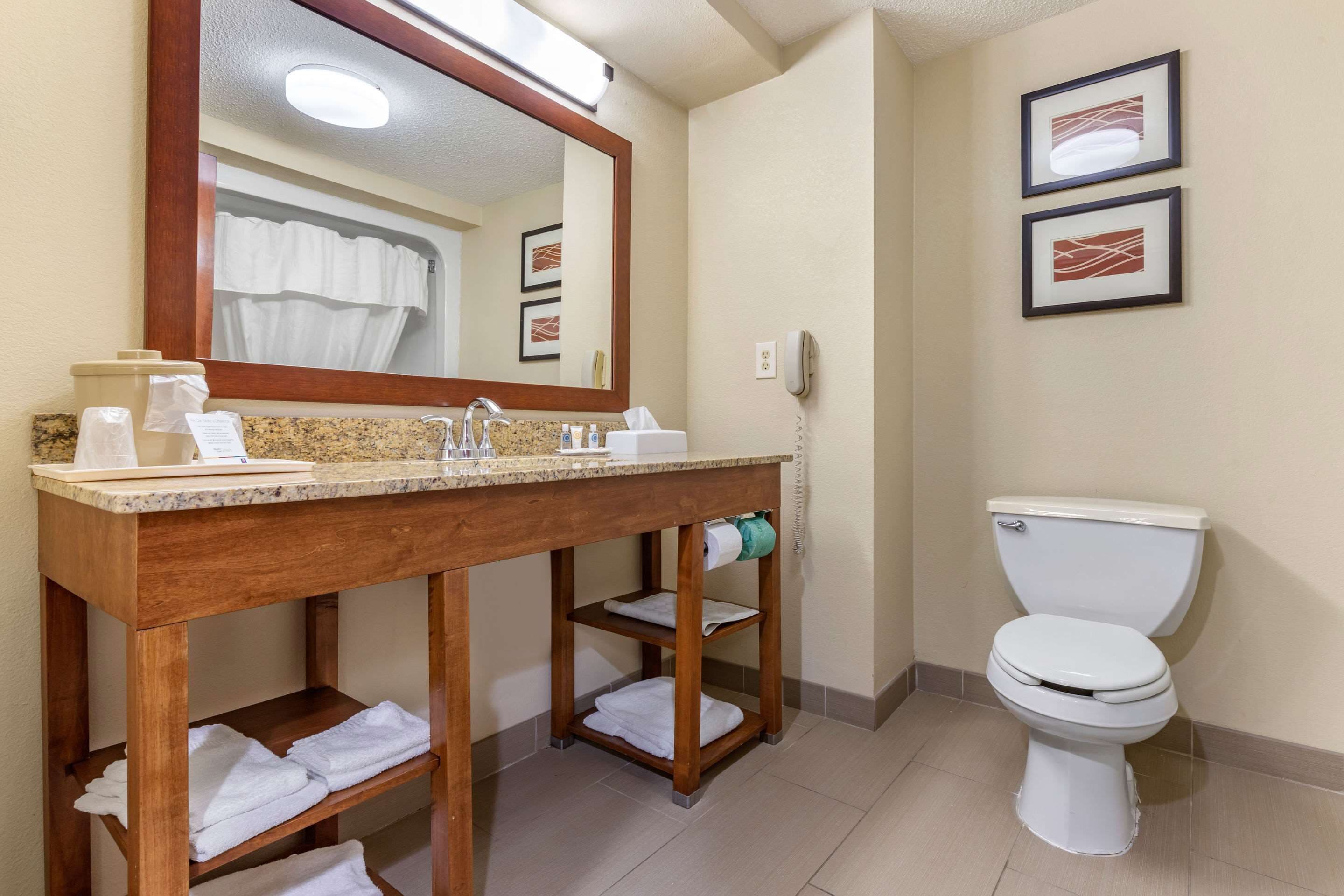 A bathroom with a wooden vanity, a sink, a mirror, a toilet, and two framed pictures on the wall.