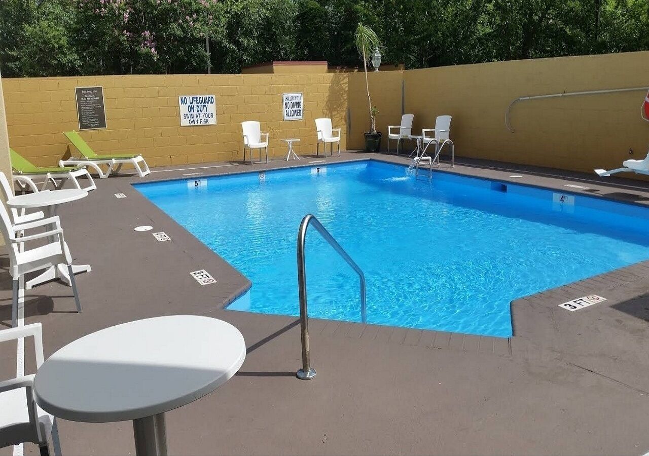 Ein Swimmingpool mit Liegestühlen und einem Tisch, umgeben von einer niedrigen Mauer und Bäumen.