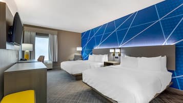 Ein Hotelzimmer mit zwei Betten, einem Schreibtisch, einem Stuhl, einem Fernseher und einem Fenster mit Vorhängen.