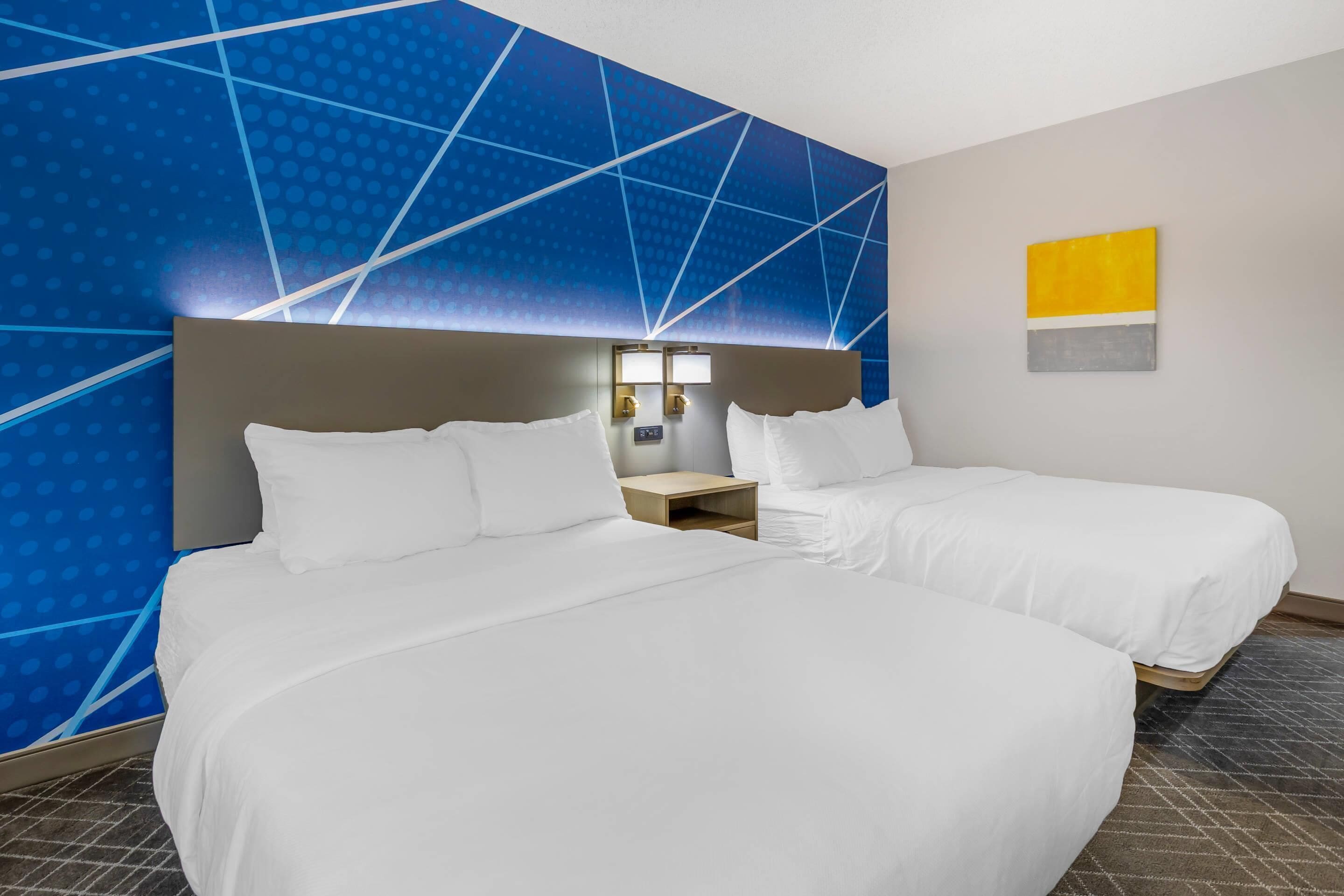 Quarto de hotel com duas camas, uma mesa de cabeceira e uma parede com padrões geométricos.
