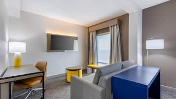 A hotel room with a desk, chair, sofa, TV, and a window with curtains.