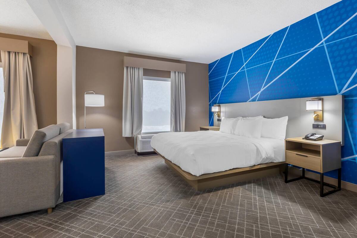Una habitación de hotel con cama, escritorio, silla y un amplio ventanal.