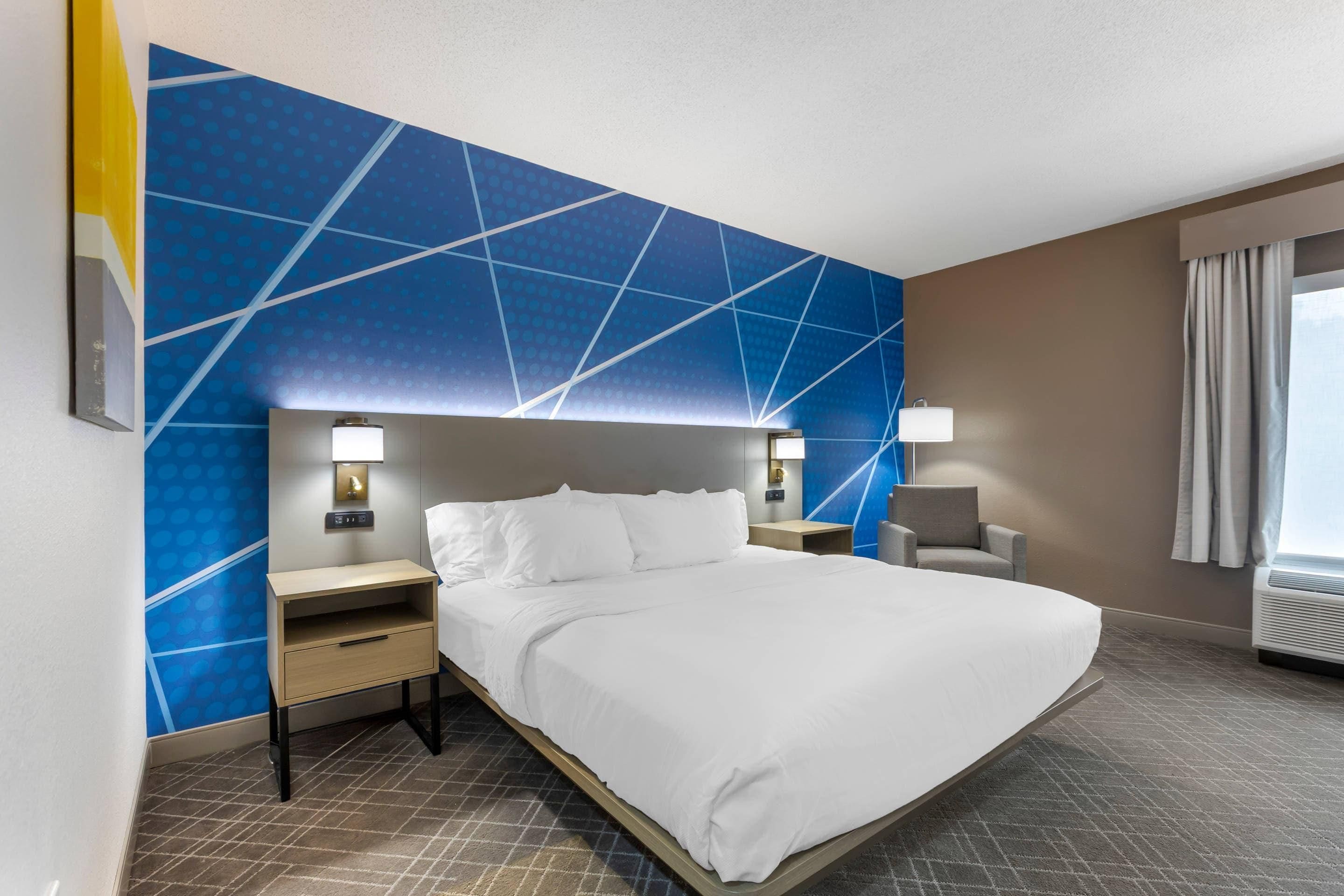 Une chambre d’hôtel avec un grand lit, deux tables de chevet, une chaise et une fenêtre avec des rideaux.