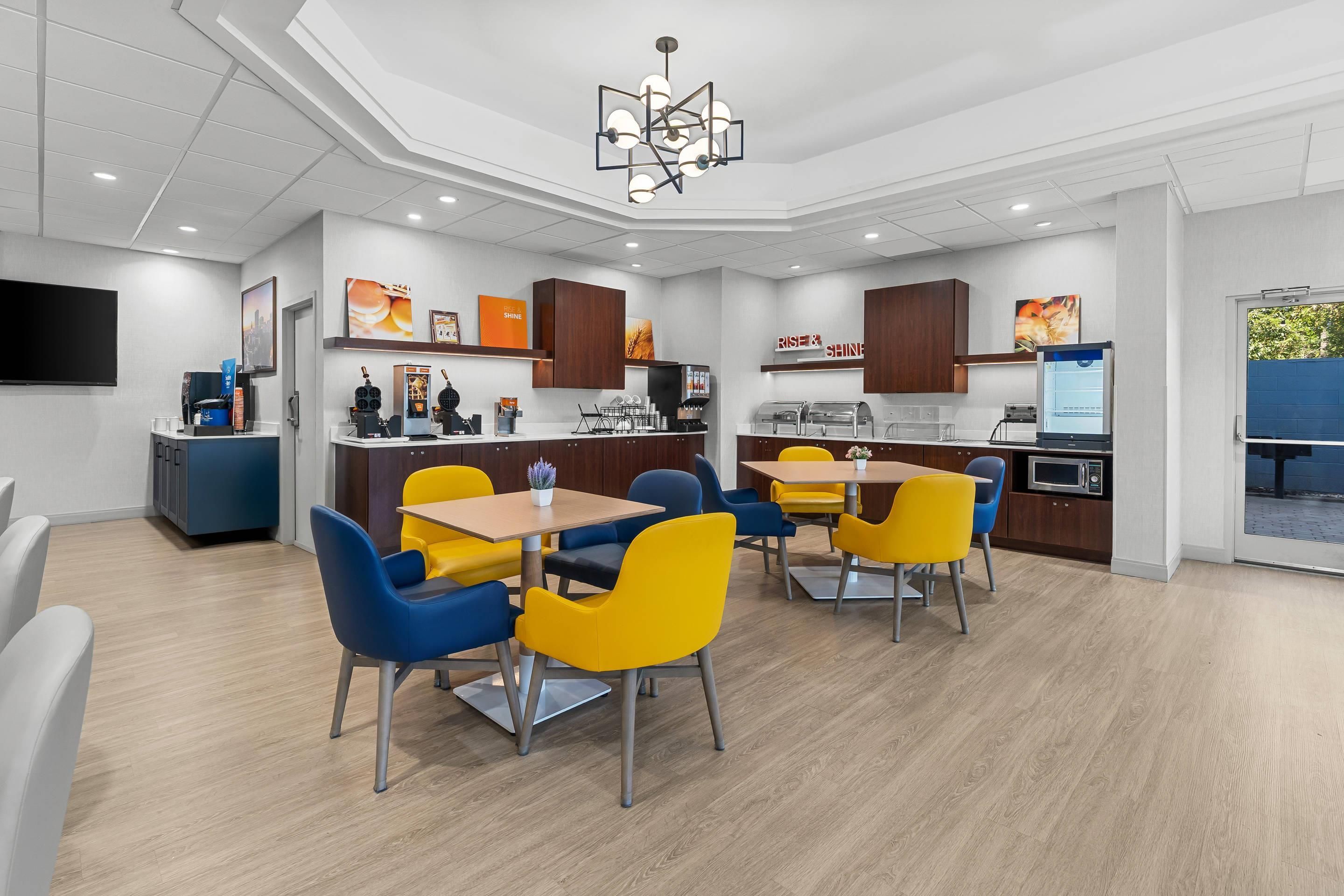 Un comedor moderno con una mesa central y sillas, una zona de cocina con electrodomésticos y un televisor de pantalla plana montado en la pared.