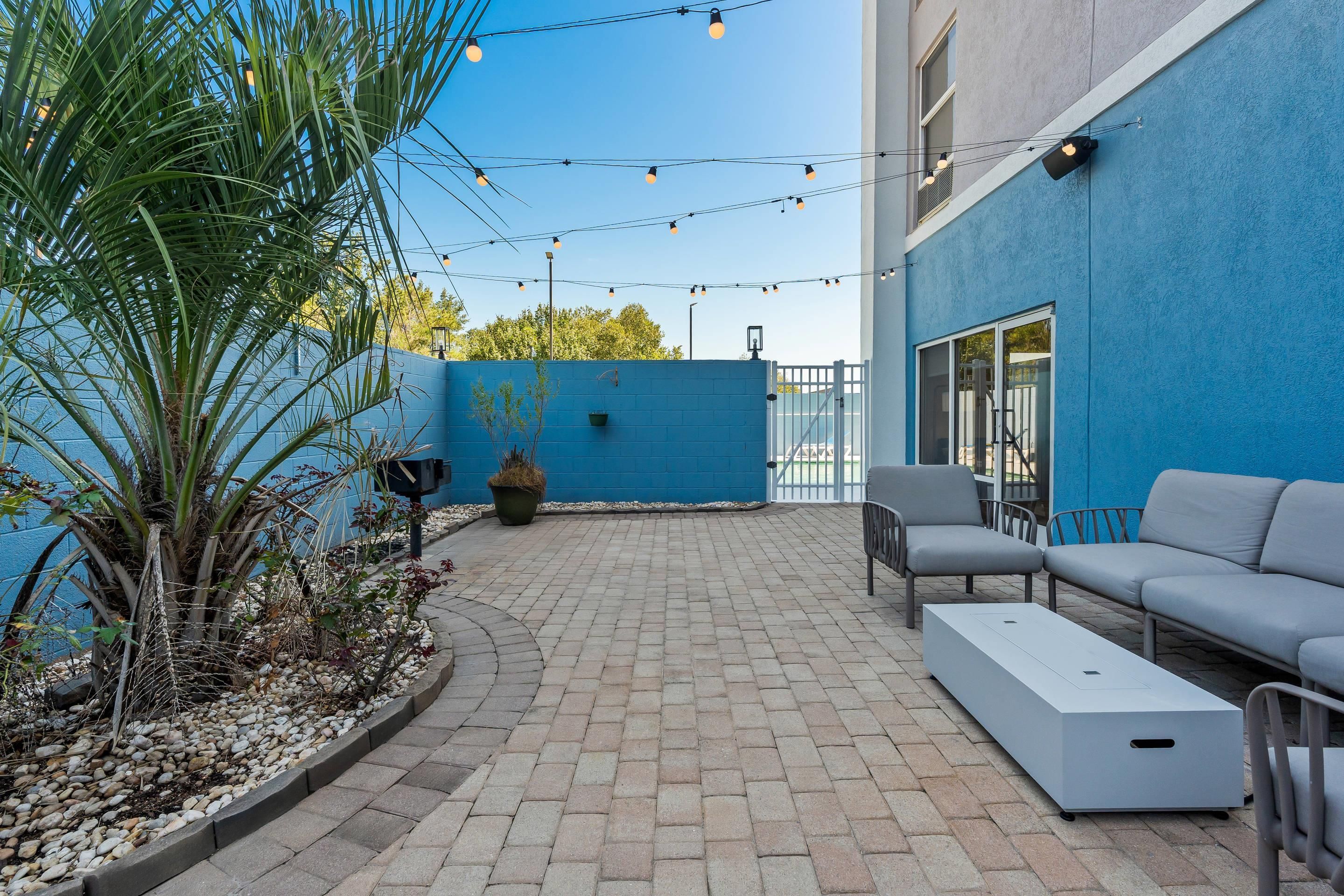 Un patio con pared azul, mobiliario exterior e iluminación con luces colgantes.