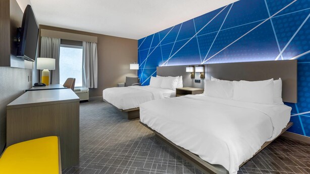 Quarto de hotel com duas camas, uma escrivaninha, uma cadeira, uma televisão e uma janela com cortinas.
