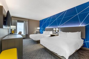 Et hotelværelse med to senge, et skrivebord, en stol, et fjernsyn og et vindue med gardiner.