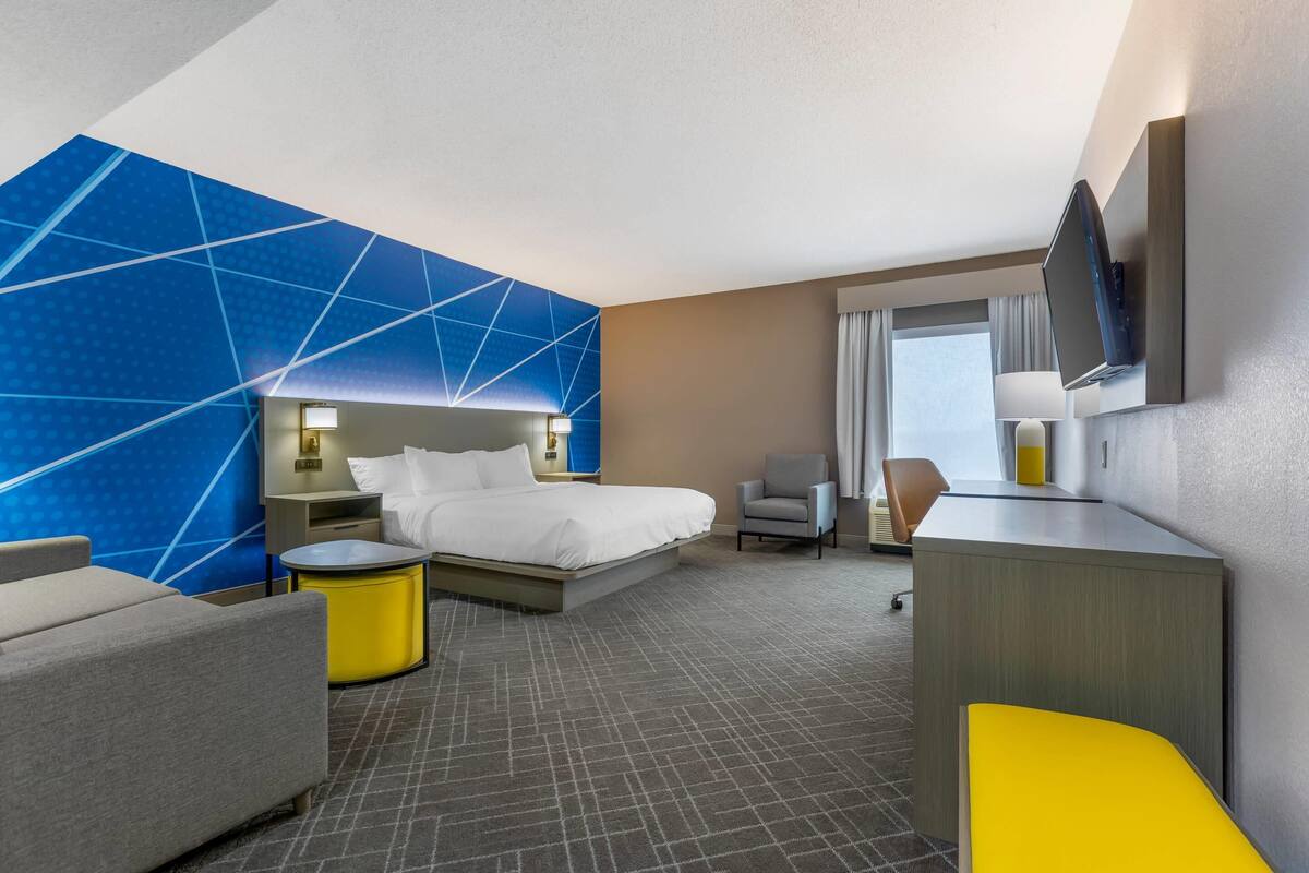 Una habitación de hotel moderna con una cama grande, un escritorio, una silla y un televisor montado en la pared.