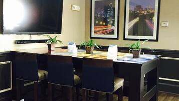 A conference room with a large flat-screen TV, a wooden table, and four chairs. There are two framed pictures on the wall and potted plants on the table.