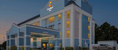 A hotel with a modern design, featuring a prominent 'Comfort Inn' sign, a covered entrance, and a parking area with a vehicle.