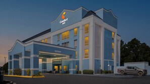 A hotel with a modern design, featuring a prominent 'Comfort Inn' sign, a covered entrance, and a parking area with a vehicle.