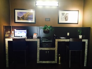 A reception desk with a laptop, a printer, and a sign indicating a business center. There are two framed pictures on the wall, one of a bridge and another of a historical figure.