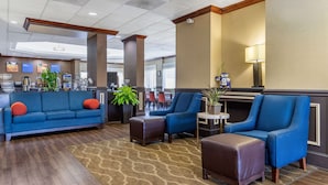 Um saguão de hotel com um sofá azul, poltronas, um espaço para café e uma área de refeições ao fundo.