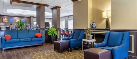 A hotel lobby with a blue sofa, armchairs, a coffee station, and a dining area in the background.