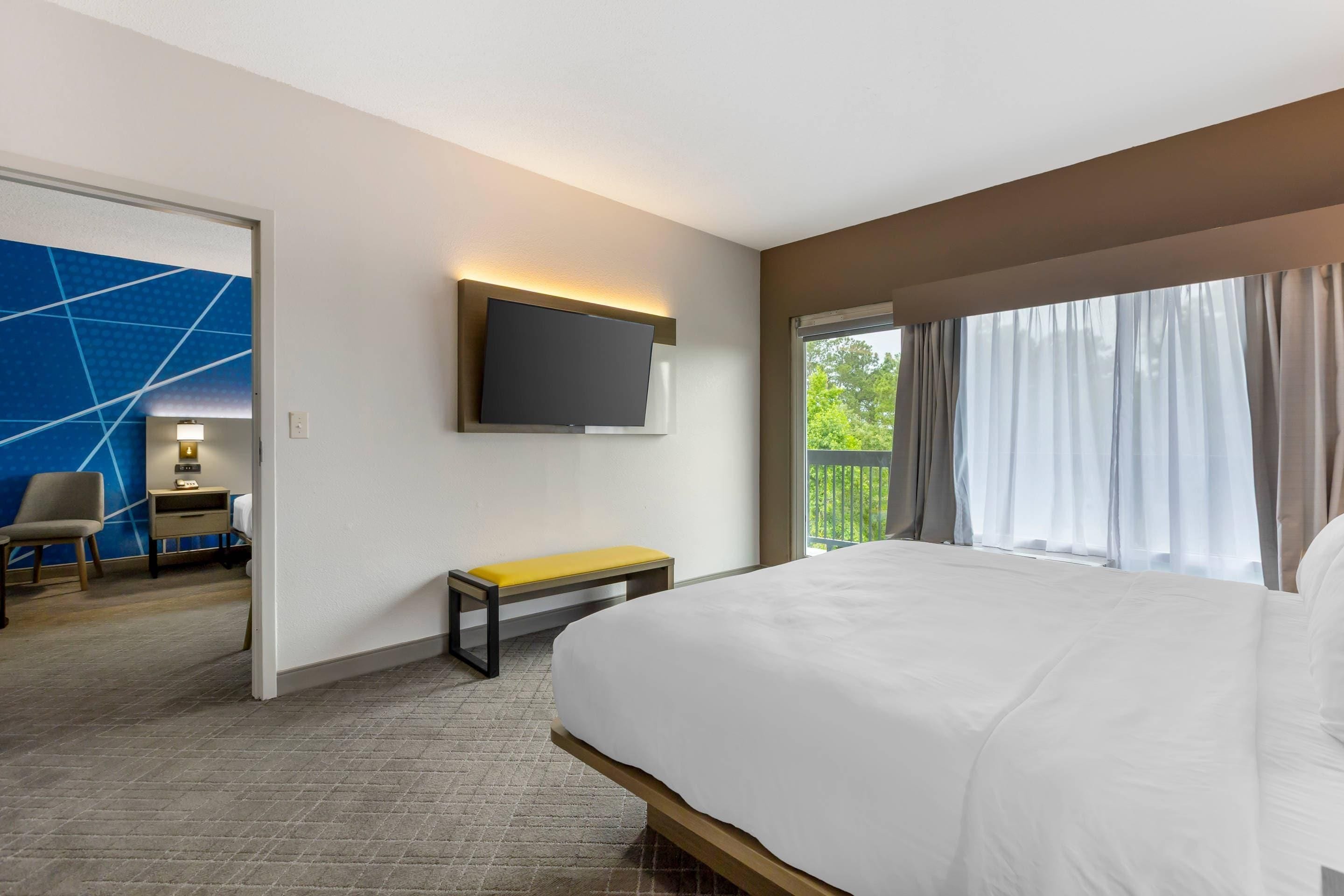 Een hotelkamer met een bed, een aan de muur bevestigde televisie, een bank en uitzicht op groen buiten het raam.