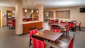 Un comedor de hotel con varias mesas y sillas, una zona de cocina y un ventanal con vistas.