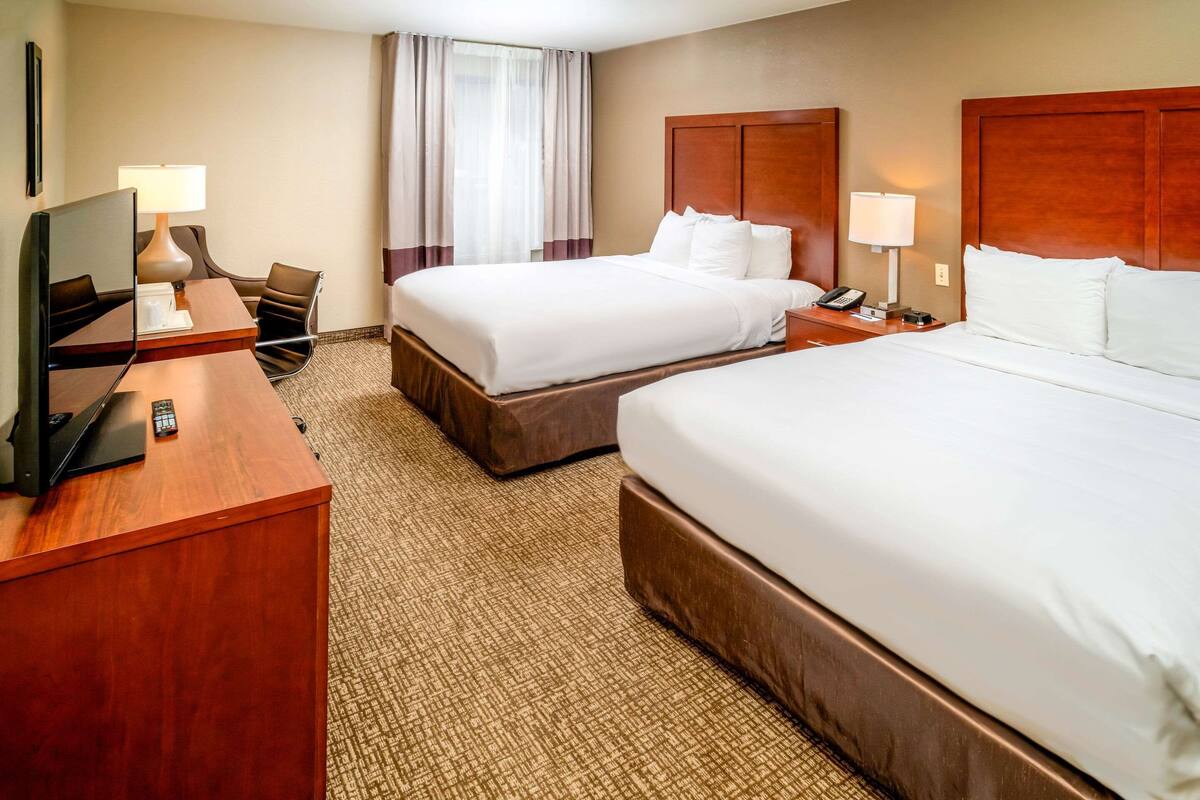 A hotel room with two beds, a desk with a television, and a chair.