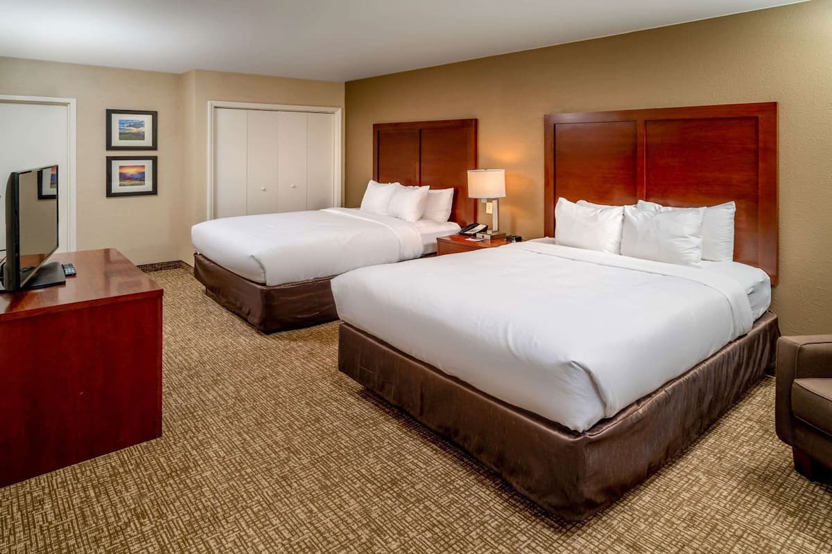 A hotel room with two beds, a desk, a TV, and a lamp.