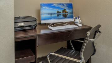 A hotel workspace with a desk, computer, chair, and two pendant lights.